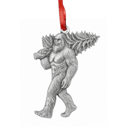 A silver metal Christmas ornament shaped like Bigfoot carrying a fern on his back, hanging from a red ribbon against a plain white background.