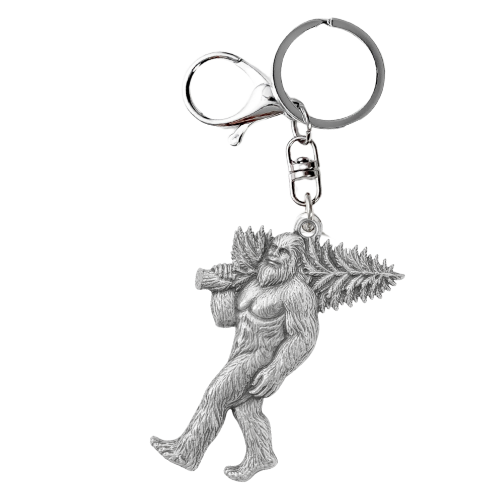 A silver metal keychain featuring a detailed figurine of a Bigfoot carrying a pine tree, attached to a classic split ring and lobster clasp, shown on a plain white background.
