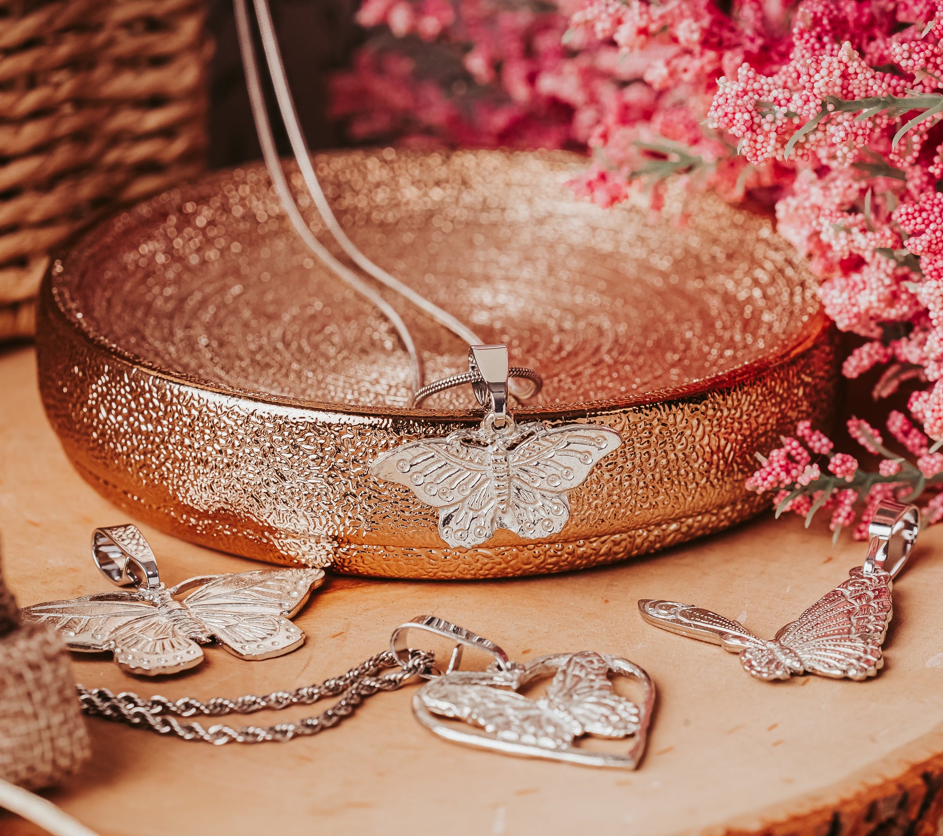 Silver butterfly pendant necklace on a decorative wooden surface with pink flowers in the background