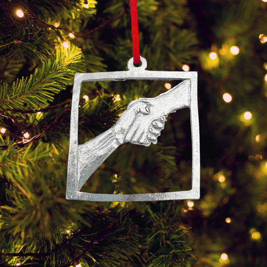 Decorative ornament of two hands shaking in a square frame hanging on a Christmas tree.