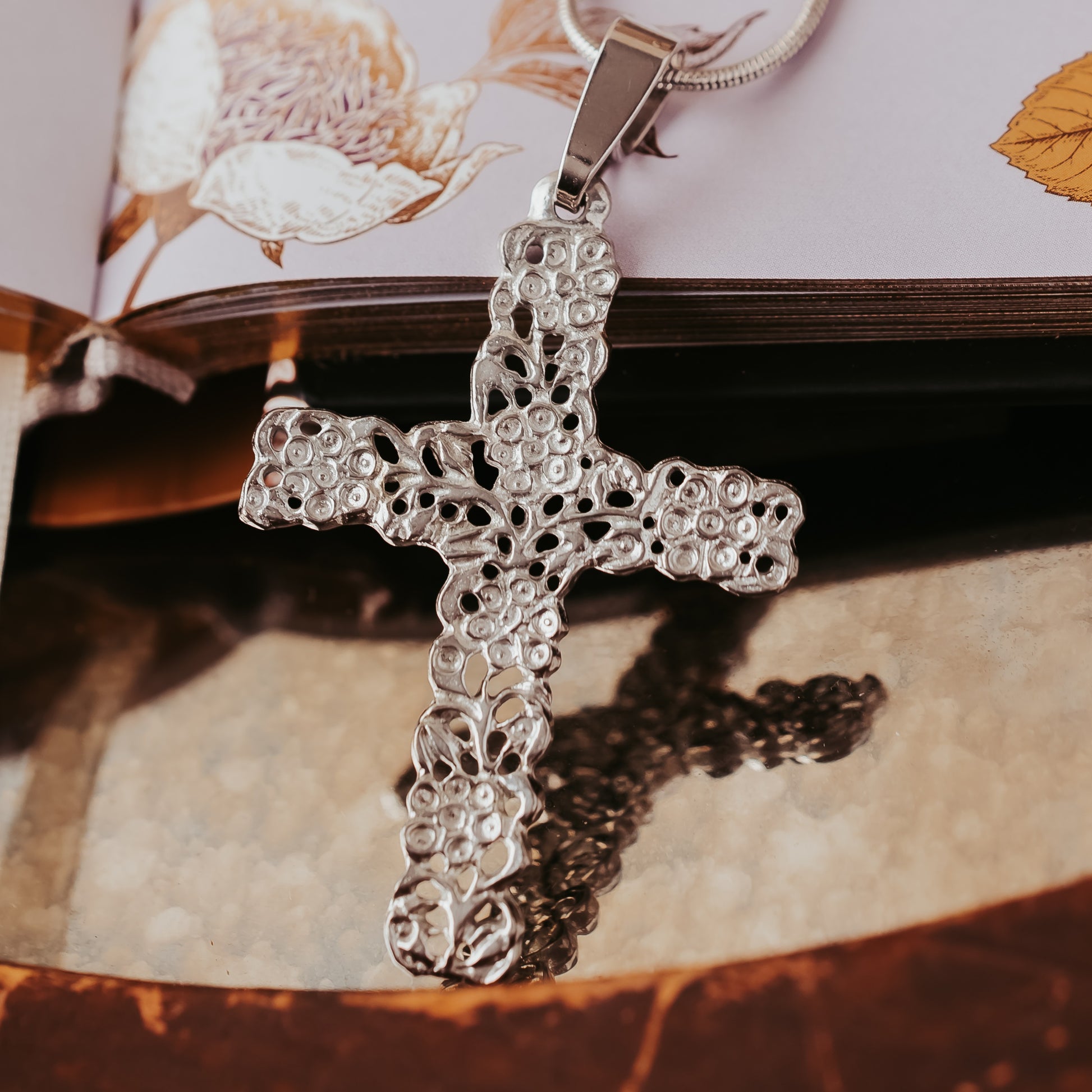 Silver cross pendant on a chain with an open book in the background