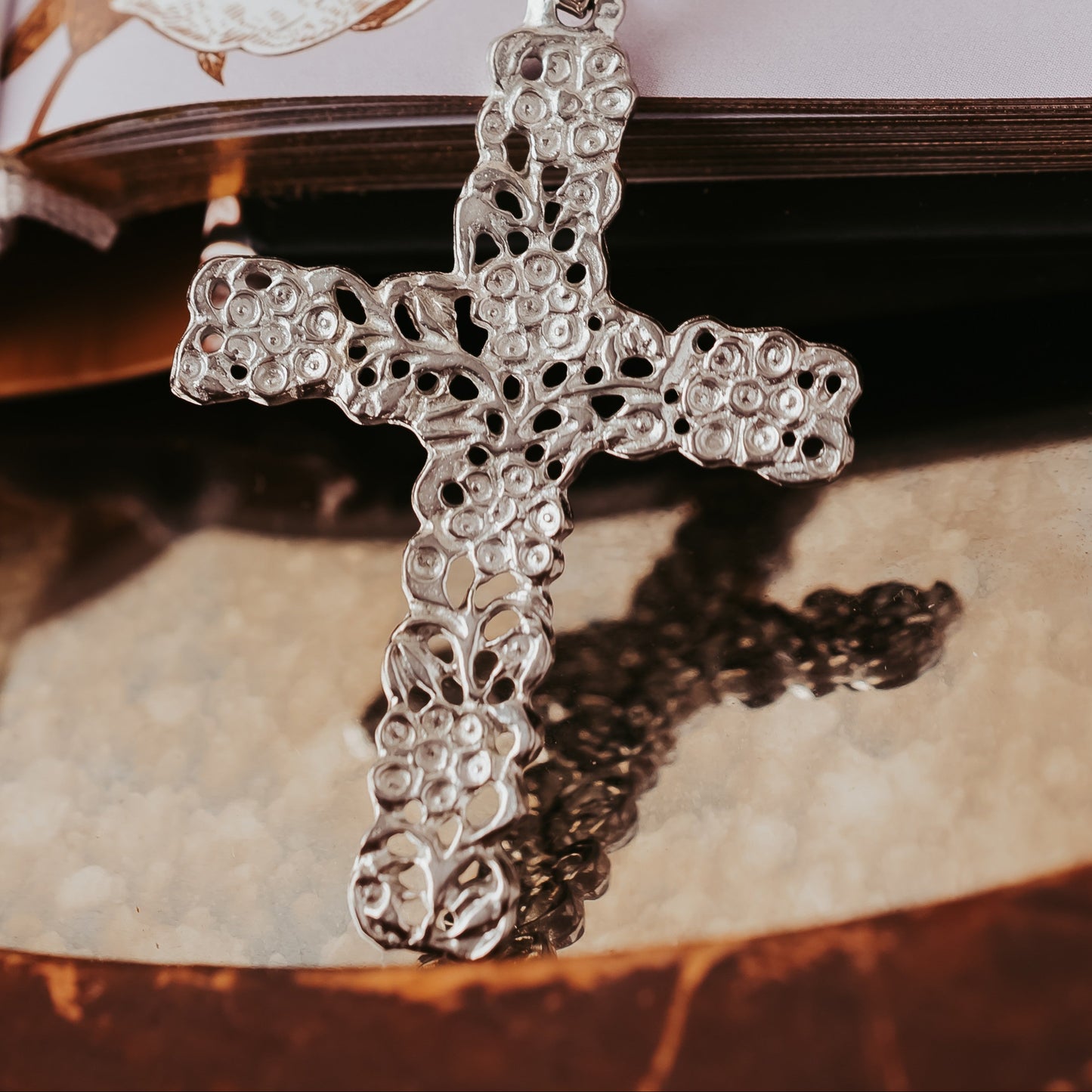 Silver cross pendant on a chain with an open book in the background