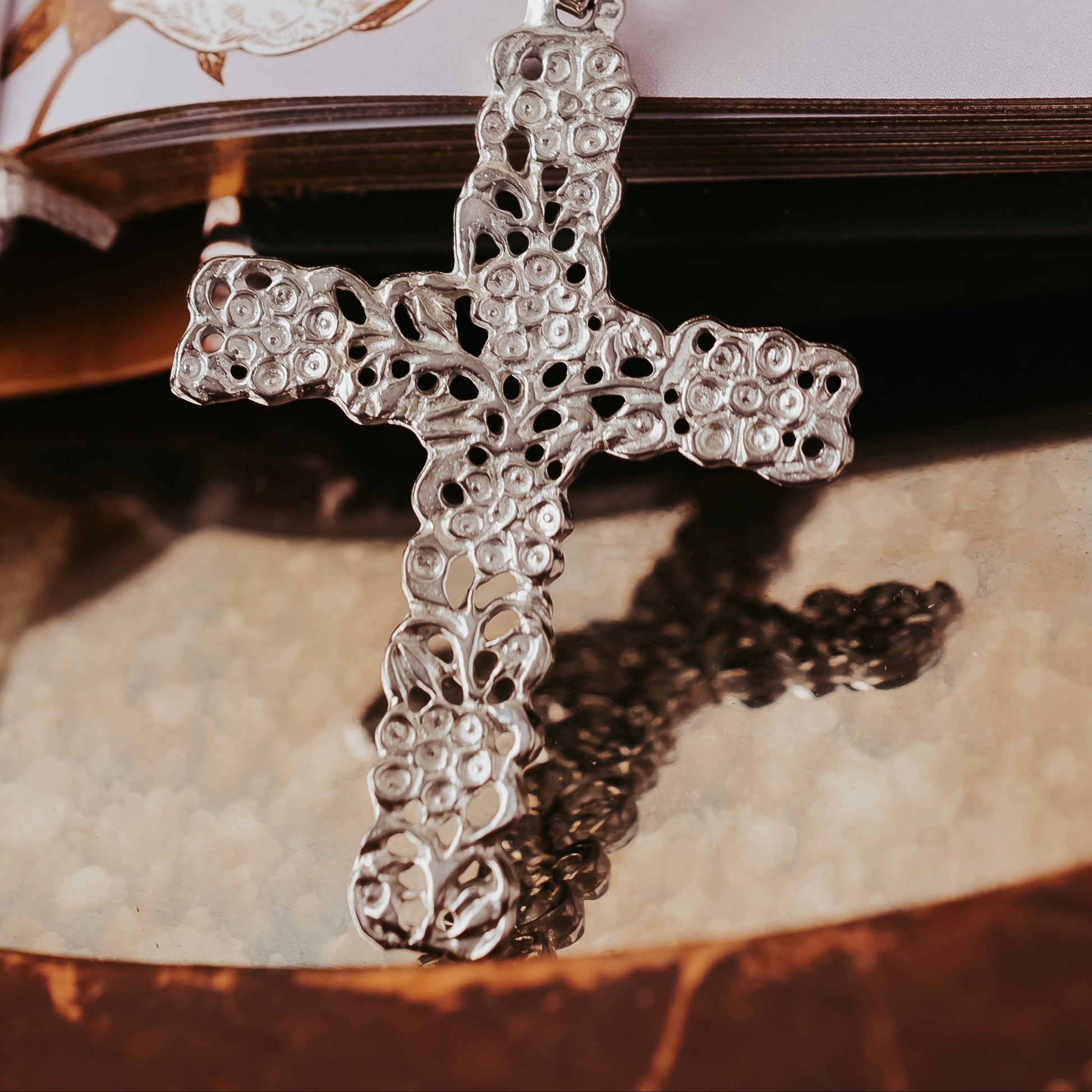Silver cross pendant on a chain with an open book in the background