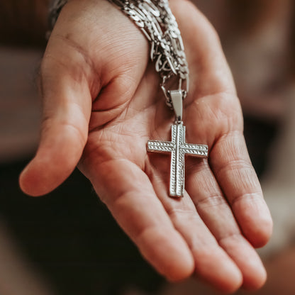 Hand holding a silver cross pendant on a blurred background