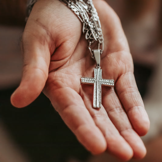 Hand holding a silver cross pendant on a blurred background
