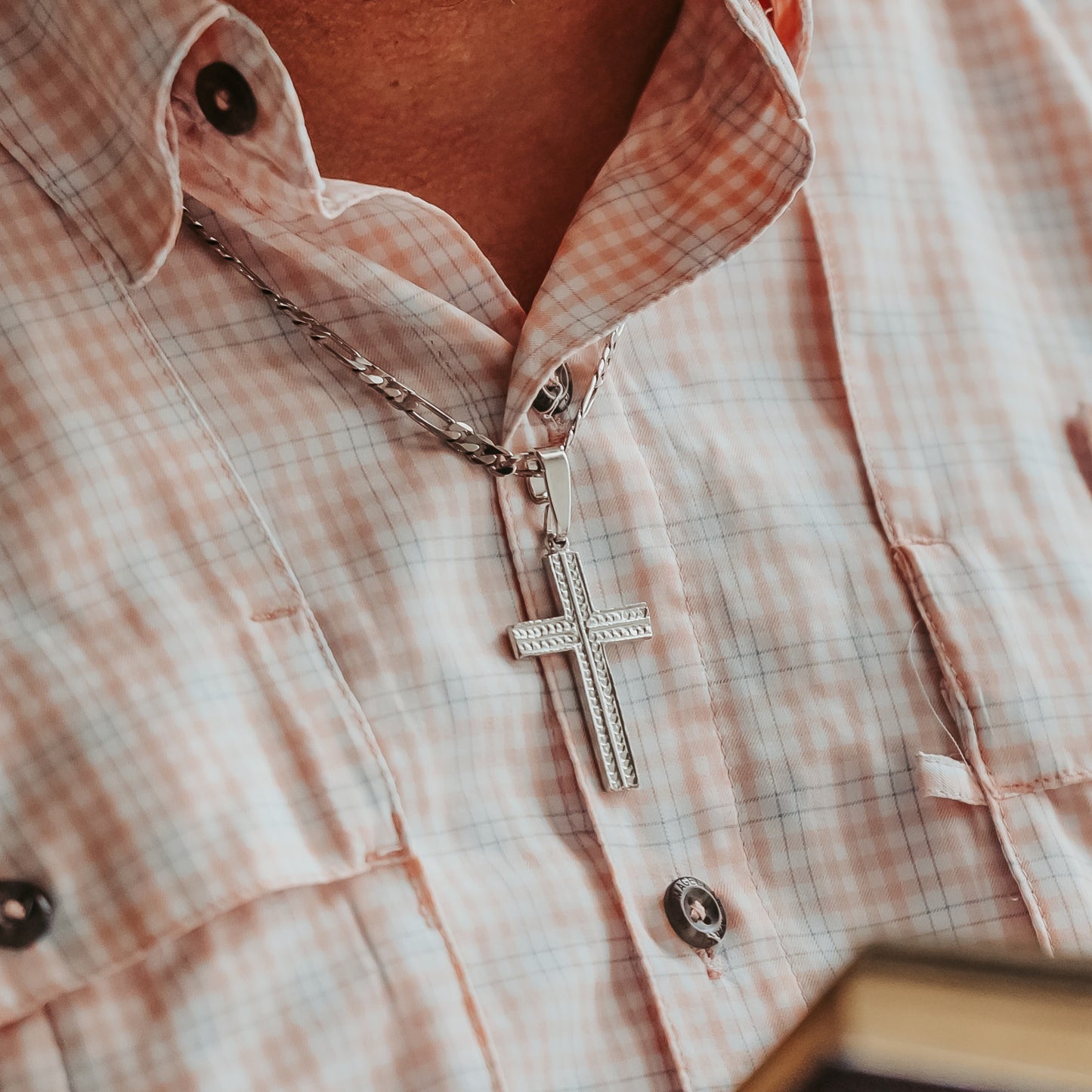 Close-up of a silver cross necklace on a plaid shirt