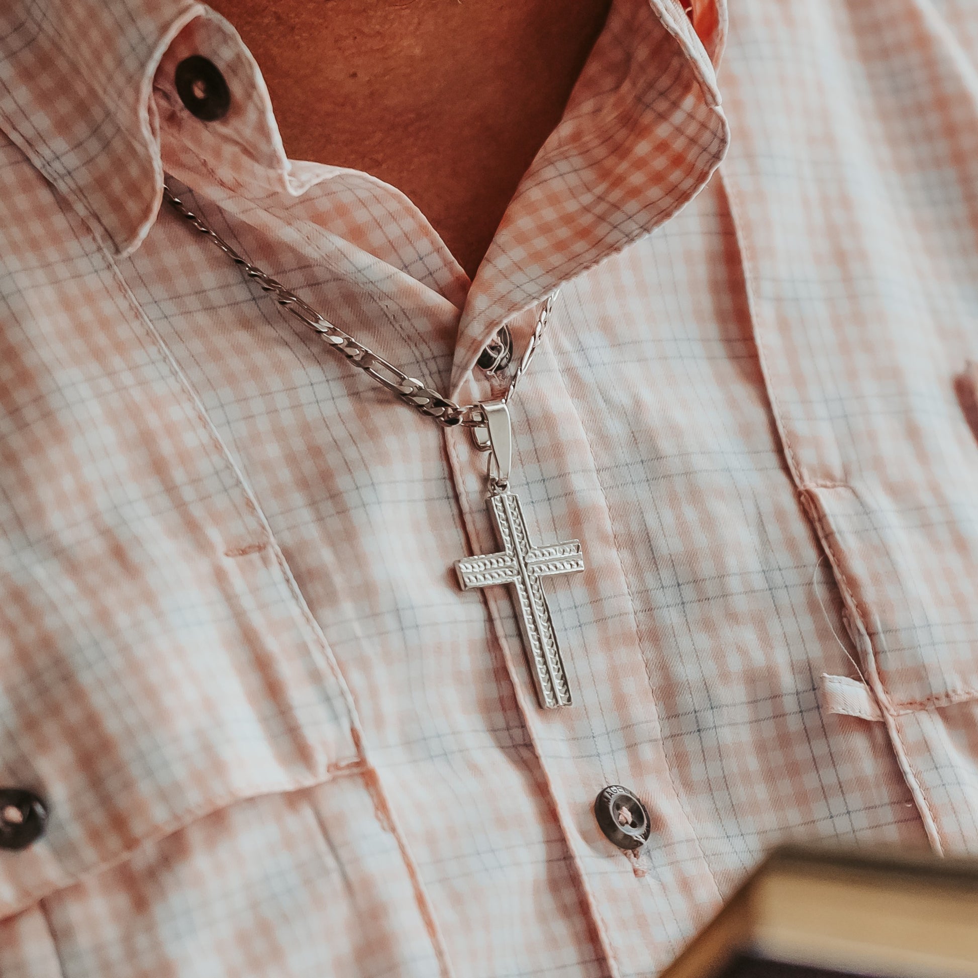Close-up of a silver cross necklace on a plaid shirt