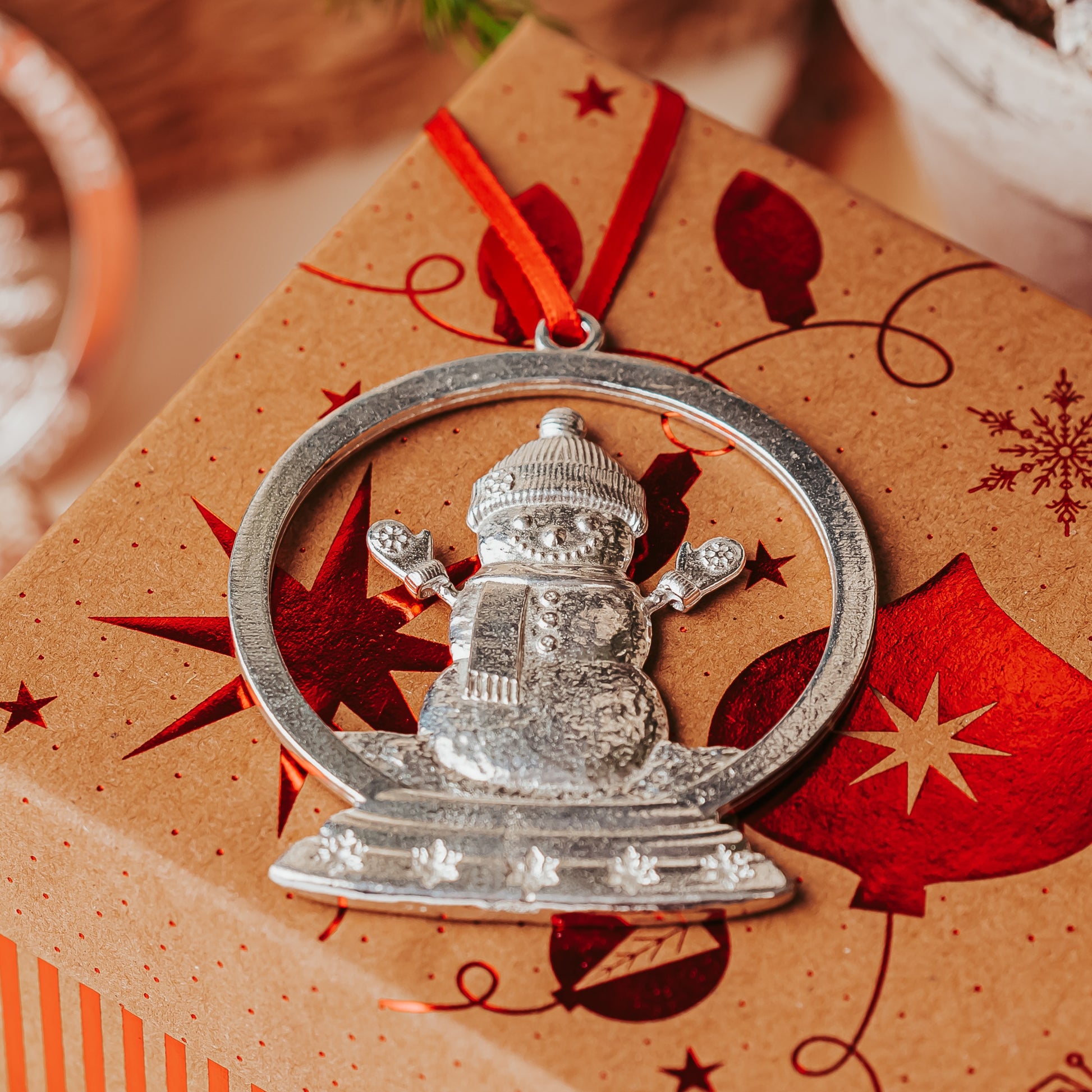 Silver snowman ornament on a decorated gift box with red ribbon