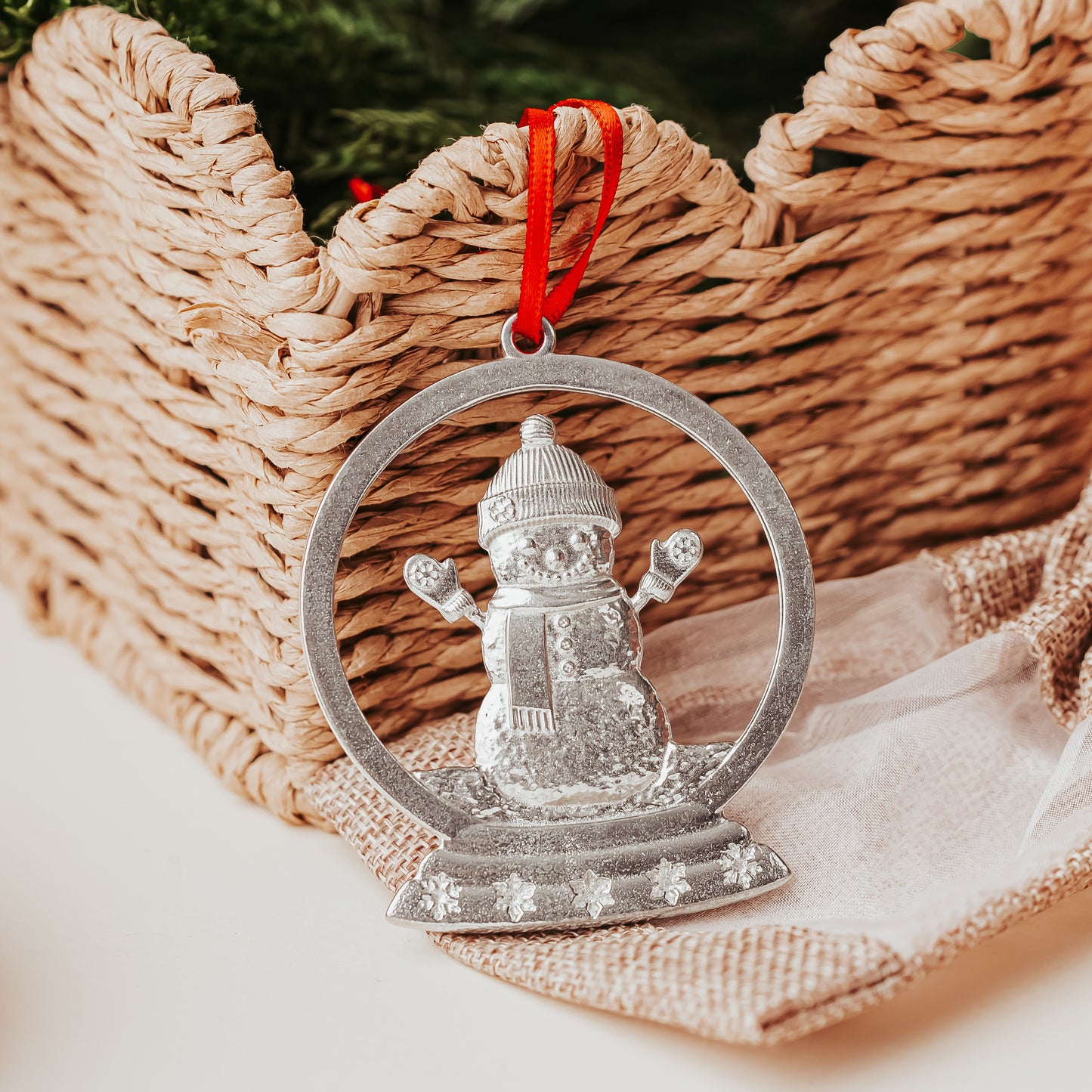 Silver snowman ornament with a red string on a woven basket background