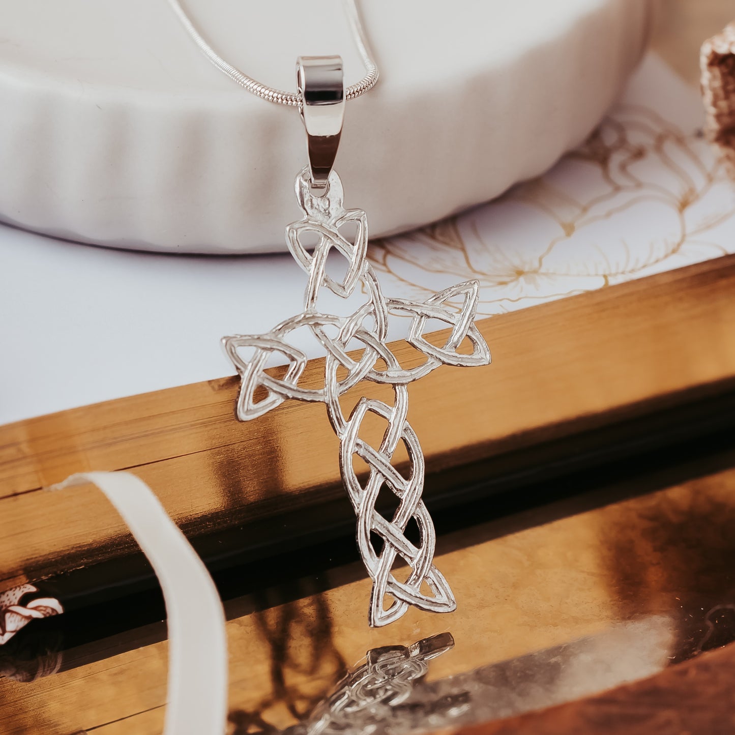 Silver Celtic cross pendant on a wooden surface with a white background